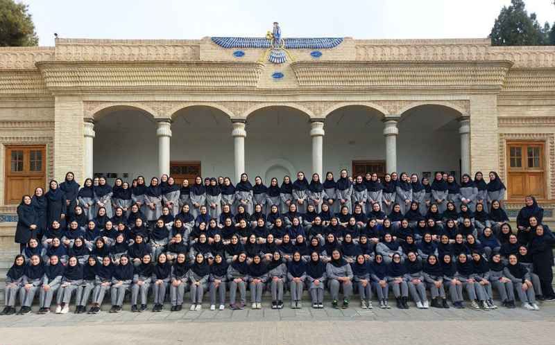 عکس گروهی رسمی از کارکنان و دانش‌آموزان مدرسه در محیط خارجی ساختمان معماری سنتی با ستون‌های سفید