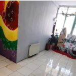 راهرویی در مدرسه با دیوار نقاشی‌شده‌ی رنگارنگ و قفسه‌های نمایش کتاب‌های مختلف