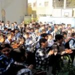 گروه بزرگی از دانش‌آموزان در حیاط مدرسه در حین برگزاری یک رویداد یا تجمع مدرسه‌ای