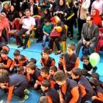 گردهمایی دانش‌آموزان در حیاط مدرسه با لباس‌های ورزشی نارنجی و آبی در یک رویداد و مراسم مدرسه‌ای