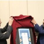 دو مسئول مدرسه در حال برداشتن پارچه قرمز از روی تابلوی شرف و لوح تقدیر در مراسم افتتاح رسمی