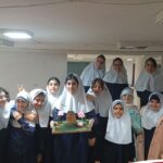 دانش‌آموزان دختر با لباس فرم سفید و مشکی در حال نمایش یک پروژه ساخت‌شده در هنگام یک رویداد یا فعالیت کلاسی
