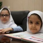 دو دانش‌آموز دختر در حال مطالعه و فعالیت گروهی درسی پشت میز در کلاس درس