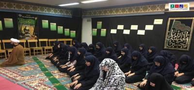 دانش‌آموزان در حال نماز در نمازخانه مدرسه با تزیینات سنتی و فرش رنگین