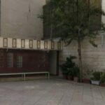 حیاط مدرسه با درخت سبز، نیمکت‌های استراحت و دیوارهای محوطه