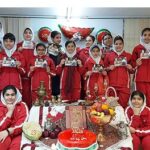 دانش‌آموزان و معلمان با لباس قرمز و سفید در حال برگزاری مراسم پرچم ملی به همراه کیک تزیین‌شده