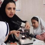 معلم و دانش‌آموز در حال انجام آزمایش علمی با میکروسکوپ در کلاس درس