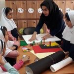دانش‌آموزان در حال انجام یک پروژه هنری تعاونی گروهی در کلاس درس، با راهنمایی مربی