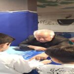 معلم و دانش‌آموزان در حال انجام یک فعالیتِ علمی عملی با دستگاه‌های آموزشی در کلاس درس