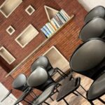 کلاس درس مدرسه با صندلی‌های مشکی، رف‌های کتاب و دیوار آجری قرمز