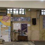 راهروی داخلی مدرسه با دیوارهای تزیین‌شده به خط‌وخطی فارسی، تابلوهای اطلاعاتی دائمی، و میز تزئینی با گل‌های تازه