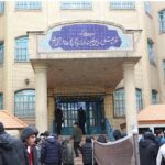 نمای بیرونی درب ورودی اصلی ساختمان مدرسه با تابلوی نام دائمی آبی و معماری داخلی کلاسیک