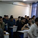 دانش‌آموزان در کلاس درسی با میزهای آموزشی و تخته سفید، دارای پنجره‌های بزرگ و نورپردازی طبیعی
