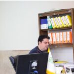 فضای اداری مدرسه با میز کار، کامپیوتر و قفسه‌های سازمان‌یافته‌ی مدارک و اسناد رنگی