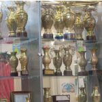 کابینت شیشه‌ای شامل مجموعه‌ای از جام‌های طلایی و نقره‌ای تقدیری و افتخاری مدرسه، نمادی از دستاوردهای تحصیلی و ورزشی