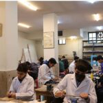 دانش‌آموزان در حال انجام آزمایش‌های علمی در آزمایشگاه، لباس کار سفید پوشیده، در کنار تجهیزات و قفسه‌های مواد شیمیایی
