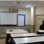 کلاس درسی مجهز به میز‌های دانش‌آموزی، تخته‌سفید و روشنایی‌های سقفی در مدرسه‌ای شهری
