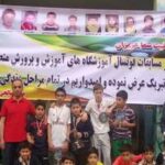 دانش‌آموزان و معلمان در حال حضور در مراسم تجلیل و تقدیر، پشت بنری که متنی از برنامه را حمل می‌کند