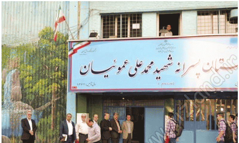 درب ورودی و نمای بیرونی ساختمان مدرسه با تابلوی نام پیشتازان پرسرائت شهید محمدی علی عسکریان و پرچم ایران