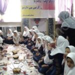 دانش‌آموزان پوشیده‌ی مدرسه‌ی دخترانه در حال صرف غذا در سالن غذاخوری با میزهای جمعی و نور طبیعی