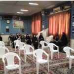 دانش‌آموزان دختر در حال شرکت در یک جلسه سخنرانی درون سالن مجهز با صندلی‌های سفید و دیوارهای آبی؛ صندلی‌های خالی در پیش‌زمینه و دستگاه پروژکتور بر روی دیوار