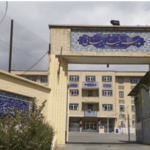 نمای ورودی ساختمان مدرسه با درب فلزی، تابلو فارسی و معماری آجری‌فیروزه‌ای