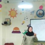 معلم در حال تدریس در کلاس درسی با تزئینات رنگی دیوار و دانش‌آموزان نشسته
