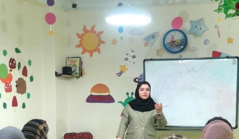 معلم در حال تدریس در کلاس درسی با تزئینات رنگی دیوار و دانش‌آموزان نشسته