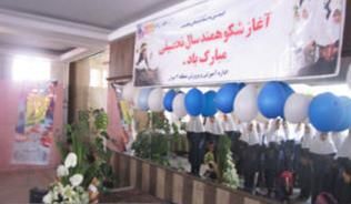 دانش‌آموزان در یک مراسم تحفل با میز تشریفات، بنرهای فارسی، گلدان‌ها و تزئینات رنگی آبی و سفید