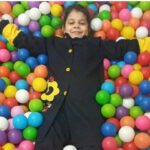 دانش‌آموز در استخر توپ رنگی‌های متعددی لبخند می‌زند — فعالیت بازی و سرگرمی در برنامه‌های مدرسه