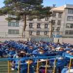 تجمع دانش‌آموزان با لباس آبی فرم مدرسه در حیاط مدرسه برای شرکت در مراسم یا فعالیت جمعی