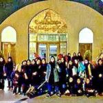 گروهی از دانش‌آموزان با لباس مدرسه در مقابل درب ورودی بنایی تاریخی با معماری سنتی ایرانی ایستاده‌اند