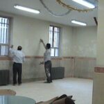دید داخلی نمازخانه مدرسه با دیوارهای سفید، پنجره‌های ایمن، و فضایی آرام و خالی