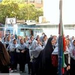 گروهی از دانش‌آموزان پوشیده با حجاب در یک مراسم یا رویداد مدرسه‌ای، با پارچه‌های تزیینی قرمز و آبی در پس‌زمینه