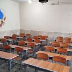 کلاس درس خالی با صندلی‌های نارنجی و میز‌های چوبی، دیوارها با تزیین آموزشی
