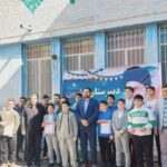 گروهی از دانش‌آموزان و معلمین در مراسم رسمی جلوی ساختمان مدرسه، برخی با حکم‌نامه و تندیس در دست