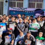 دانش‌آموزان و معلمان مدرسه در حیاط، در حال شرکت در مراسم تشریف و دریافت گواهی‌نامه‌های پایان سال