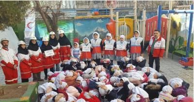 گروه بزرگی از دانش‌آموزان با لباس‌های قرمز و سفید در حیاط مدرسه در حین یک مراسم یا رویداد تشکیل‌دهندگی