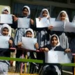 دانش‌آموزان دختری مدرسه در حال نمایش پروژه‌ها و مدارک آموزشی در یک رویداد مدرسه‌ای
