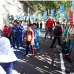 دانشآموزان در حین شرکت در یک فعالیت ورزشی گروهی در حیاط، لباس ورزشی رنگین پوشیدهاند و تابلوهای رنگی برای تزئین استفاده شده است