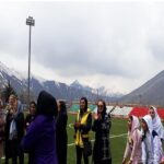 دانشآموزان دختر ایرانی در حال شرکت در فعالیت رویدادی در زمین فوتبال سالن ورزشی مدرسه، کوههای برفانی در پسزمینه