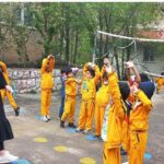دانشآموزان در حال بازی والیبال در حیاط مدرسه با راهنمایی مربی