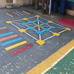 حیاط مدرسه با بازی‌های هندسی و ریاضی رنگی رسم شده روی زمین، شامل خطوط رنگین، شبکه‌های هندسی و اشکال هندسی مختلف برای فعالیت‌های آموزشی و بازی دانش‌آموزان
