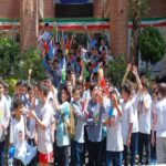 دانش‌آموزان مدرسه در حیاط هنگام مراسم ملی، برخی با پرچم‌های رنگین سبز و قرمز در دست، گروهی دیگر روی بالکنی‌های ساختمان