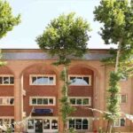 نمای بیرونی ساختمان اصلی مدرسه با معماری خشتی، پنجره‌های متعدد و فضای سبز