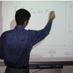 دانش‌آموز دختر یا پسری در حال نوشتن و تعامل با صفحه نمایش تعاملی در کلاس انفورماتیک یا سایت کامپیوتر مدرسه