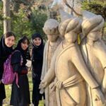 دانش‌آموزان دختر در کنار پیکره‌های سنگی در فضای باز حیاط