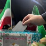 دانش‌آموزی در حال ریختن بطاقه رای خود به صندوق رای در انتخابات شورای دانش‌آموزی، با پرچم ملی ایران در پس‌زمینه