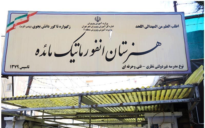 درب و تابلوی ورودی مدرسه با نوشته‌های رسمی و لوگوی ملی، نمای بیرونی ساختمان
