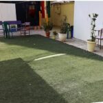 حیاط داخلی مدرسه با چمن مصنوعی، صندلی‌های رنگی و گلدان‌های گل